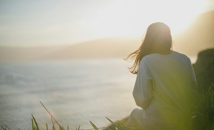 A woman standing calmly facing the sea, reflecting mental health awareness and wellbeing