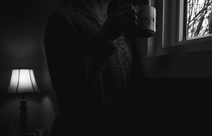 Winter blues and the clocks going back A woman looking out of a window with a warm drink on a grey winter morning
